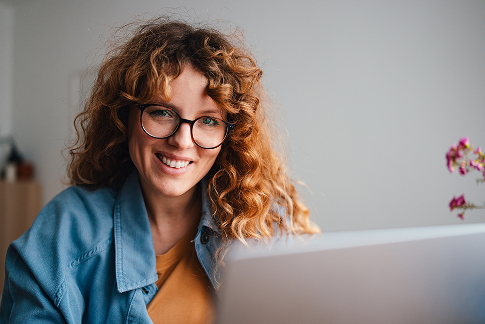 Eine Frau mit lockigen Haaren und Brille sitzt vor einem Laptop, als Symbolbild für Arbeitgeber der Zukunft